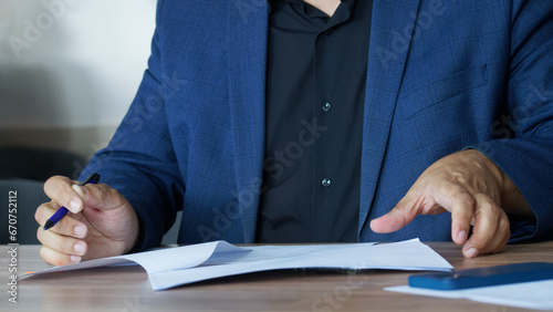 Photos An adult man in a business suit, sitting at a table with a pen, fills out an agreement or order form
