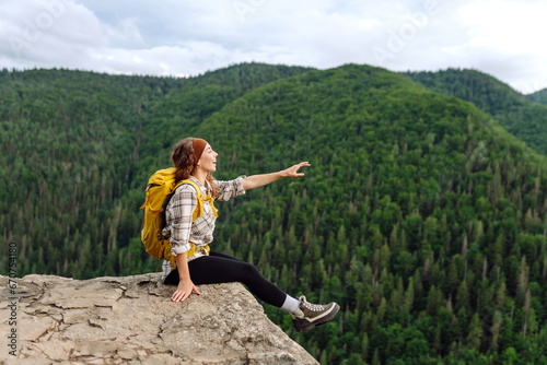 An active woman with a yellow backpack travels through the mountains. A young traveler on a cliff enjoying the sight of a Slovak troll. Travel concept.