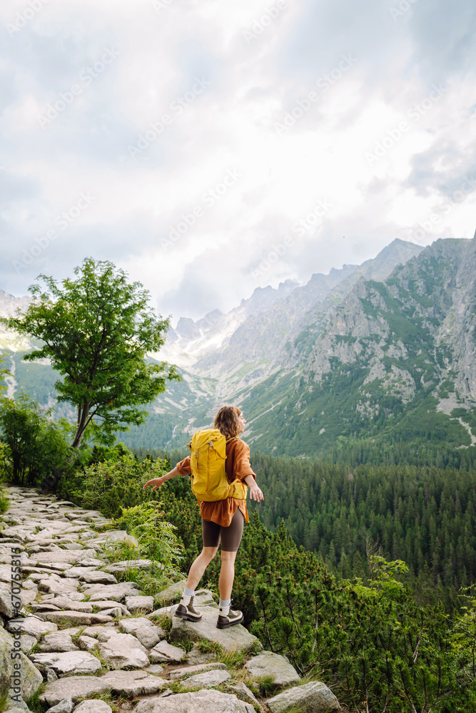 Naklejka premium Young traveler woman with a yellow backpack on a cliff enjoying mountain views. Sports concept, traveler. Active lifestyle.