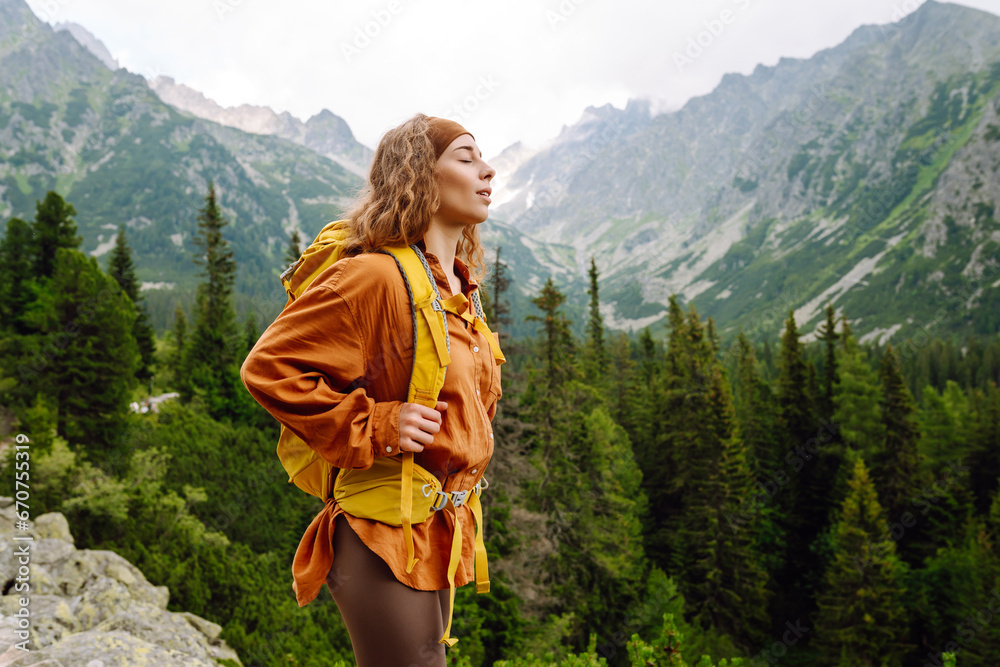 Young traveler woman with a yellow backpack on a cliff enjoying mountain views. Sports concept, traveler. Active lifestyle.