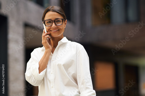 Smiling female sales manager talking phone with client while standing in coworking 