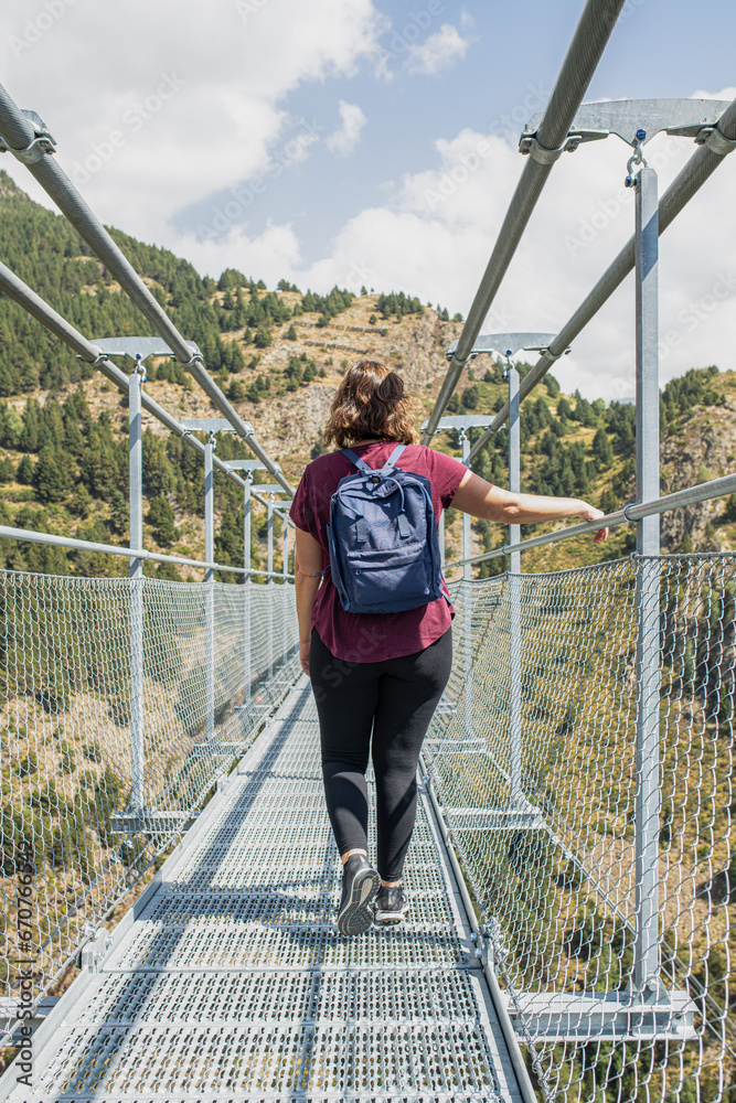 young caucasian girl on her back enjoying a quiet walk along the long hanging metal bridge between the mountains holding on to the railing in canillo andorra pyrenees young caucasian girl on her back enjoying a quiet walk along the long hanging metal bridge between the mountains holding on to the railing in canillo andorra pyrenees