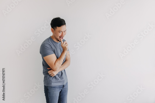 Evil looks of asian man in blue t-shirt smile and smirk stand isolated on white. photo