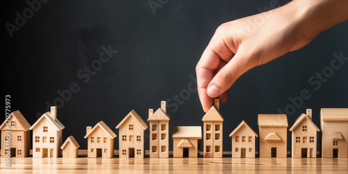 Housing market crisis – showing small toy wooden block houses with hands adjusting and placing coins on top photo