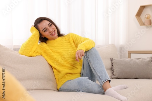 Beautiful young woman in stylish warm sweater on sofa at home