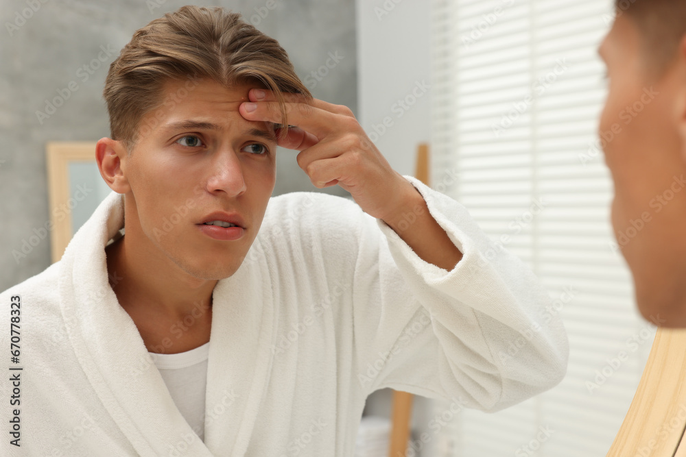 Upset young man looking at mirror and touching pimple on his face indoors. Acne problem Upset young man looking at mirror and touching pimple on his face indoors. Acne problem