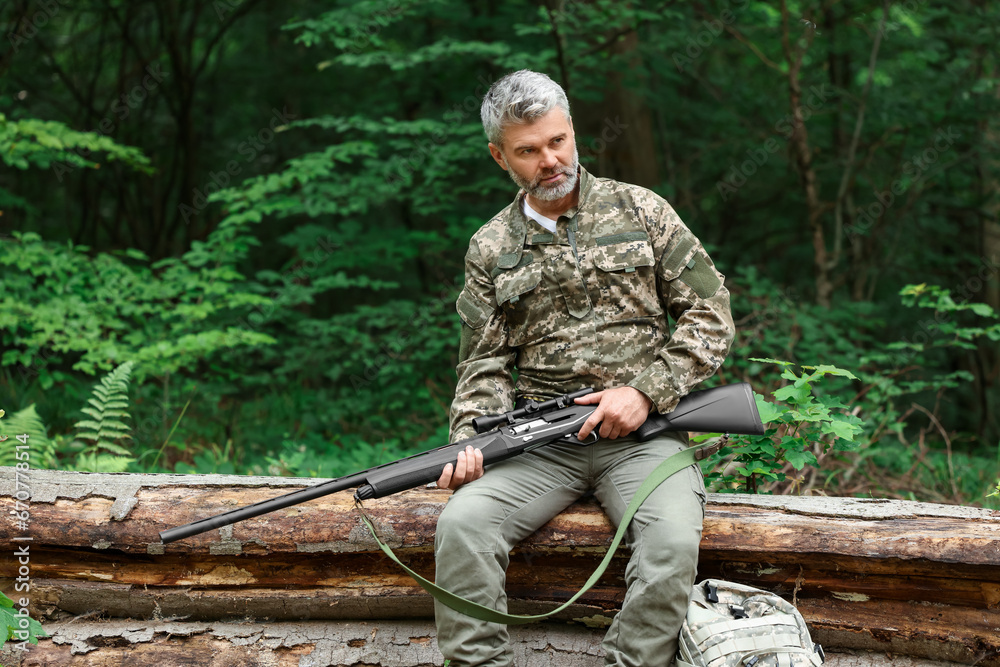 Man with hunting rifle sitting on fallen tree in forest. Space for text