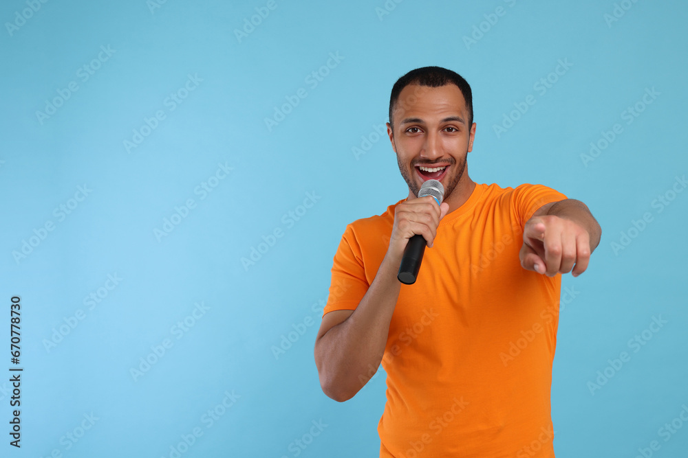 Handsome man with microphone singing on light blue background, space for text Handsome man with microphone singing on light blue background, space for text