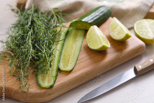 Fresh tarragon leaves, cucumber, lime and knife on white wooden table, closeup