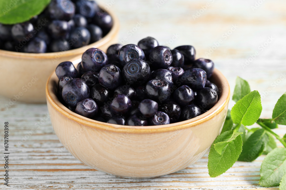 Bowls with tasty fresh bilberries and leaves on old light blue wooden table, closeup Bowls with tasty fresh bilberries and leaves on old light blue wooden table, closeup