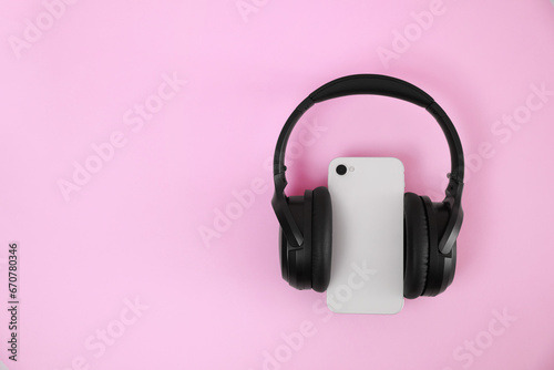 Modern wireless headphones and smartphone on pink background, top view. Space for text