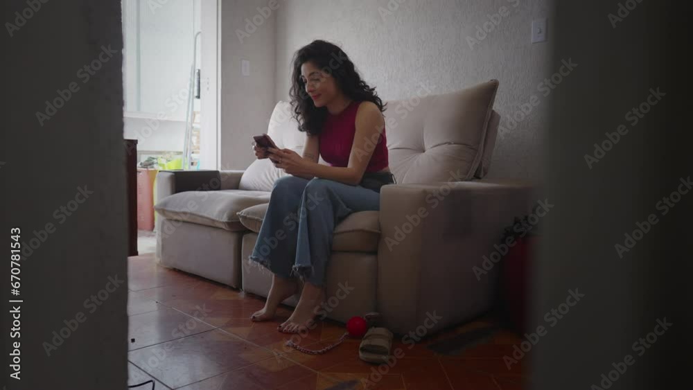 Happy woman checking phone sitting on couch at home apartment. 30s female person looking at cellphone screen browsing internet