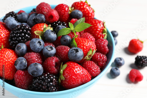 Many different fresh ripe berries in bowl on white wooden table  closeup