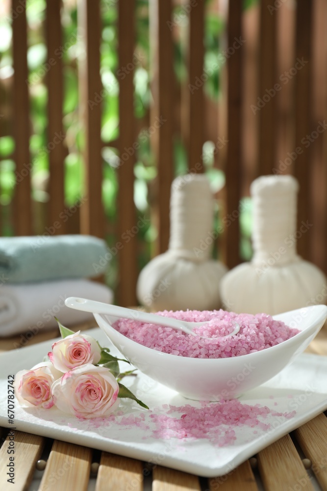 Bowl of pink sea salt and beautiful roses on wooden table, space for text Bowl of pink sea salt and beautiful roses on wooden table, space for text