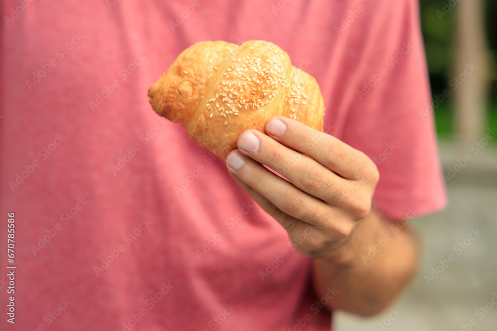 Guy's hand holds a croissant, snack and fast food concept. Selective focus on hands with blurred background Guy's hand holds a croissant, snack and fast food concept. Selective focus on hands with blurred background