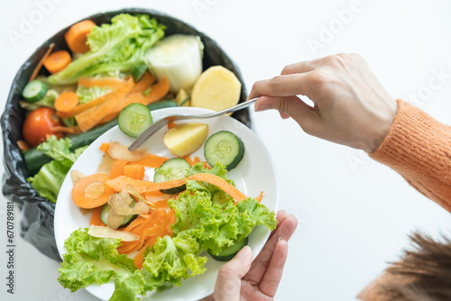 Compost from leftover food, asian young housekeeper woman hand holding plate use fork scraping waste, rotten vegetable throwing away into garbage, trash or bin. Environmentally responsible.