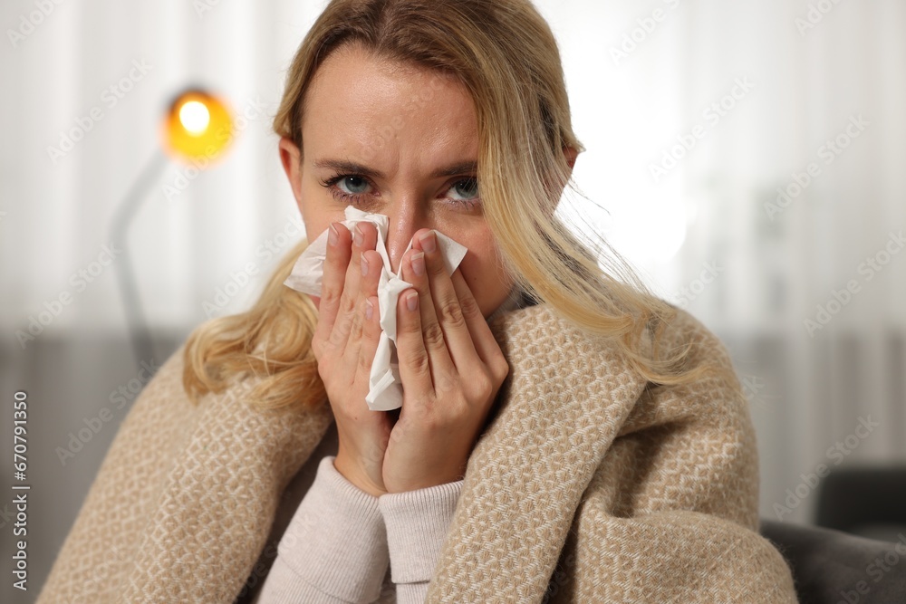 Sick woman wrapped in blanket blowing nose in tissue at home. Cold symptoms Sick woman wrapped in blanket blowing nose in tissue at home. Cold symptoms