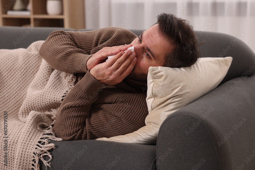 Sick man with tissue blowing nose on sofa at home. Cold symptoms Sick man with tissue blowing nose on sofa at home. Cold symptoms