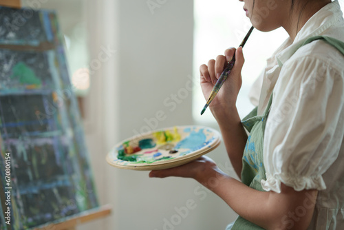 Young Asian female artist holds a palette with mixed acrylic paints. Use your creativity in designing pictures. Create art on canvas Develop art drawing skills Hobby activities in the studio or home.