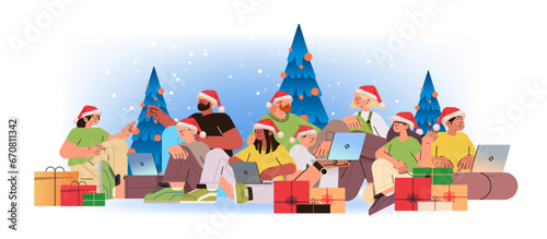 mix race men women in santa hats near decorated christmas tree using laptops social media communication new year holidays celebration