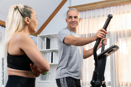 Active senior couple running on elliptical running machine at home together as fitness healthy lifestyle and body care after retirement for pensioner. Clout