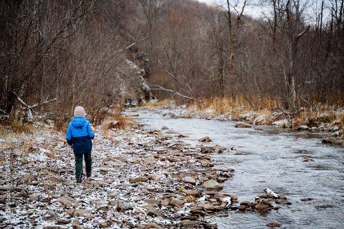 Little boy walking alone along a frozen river, hiking in nature, mountain stream, first day of winter, child wandering alone on stones.