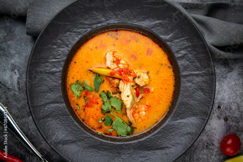 Tableau sur toile spicy tom yum in a black plate with greens, top view
