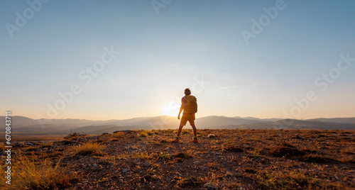 An active young man feels free. A confident man stands on a mountain against the background of a sunset. Experience freedom in the heart of nature.