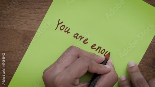 Affirmation of Self-Worth: Top-View of Hands Writing 'You Are Enough' on Green Paper