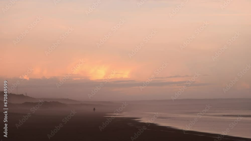 Man taking a peaceful walk at the end of the day on the beach in the fog with colorful reflections, 4K Man taking a peaceful walk at the end of the day on the beach in the fog with colorful reflections, 4K