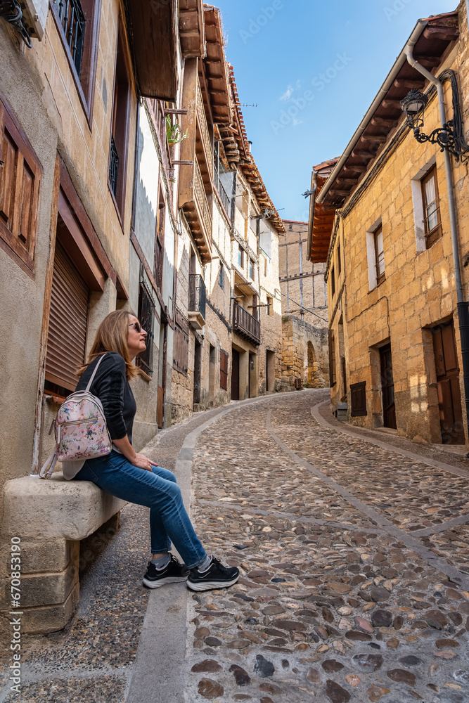 Tourist woman resting on a stone bench in the medieval town of Frias, Burgos, Spain.