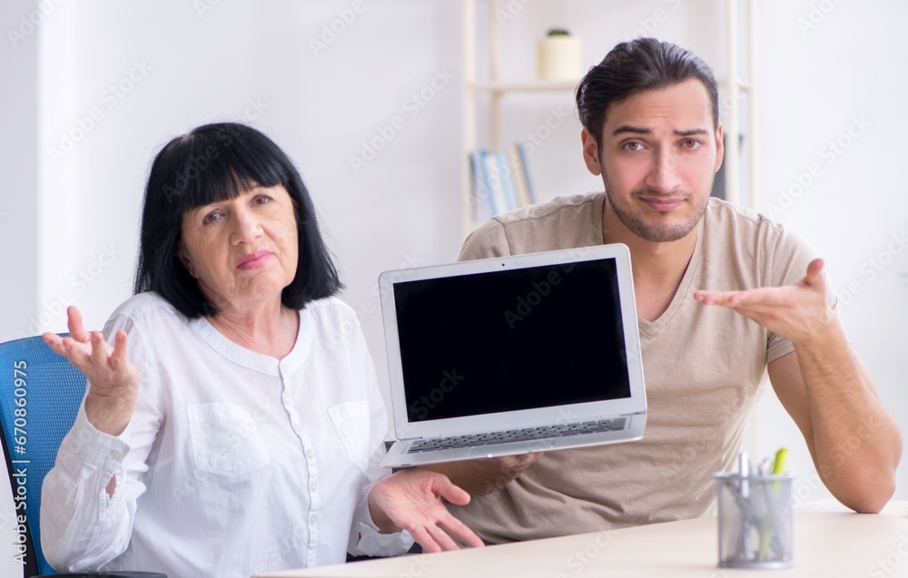 Young male employee explaining to old female colleague how to us Young male employee explaining to old female colleague how to us