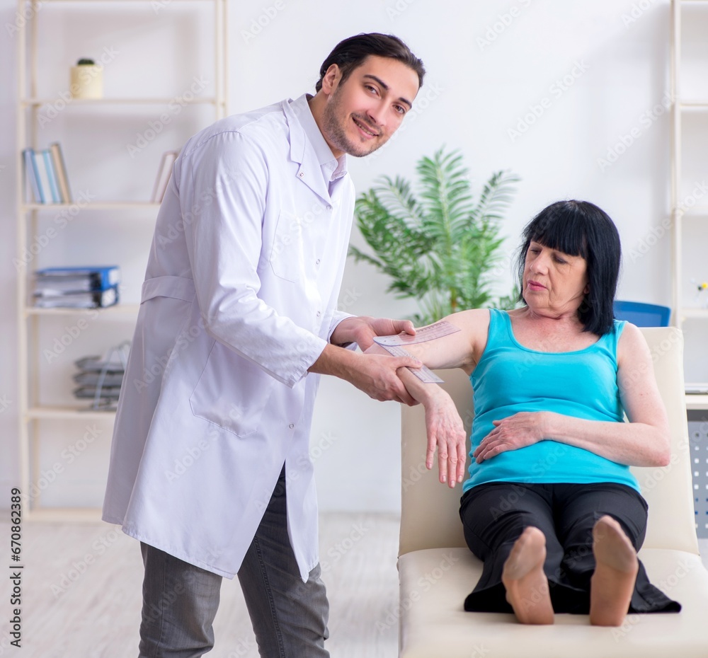 Fototapeta premium Young male doctor examining old female patient