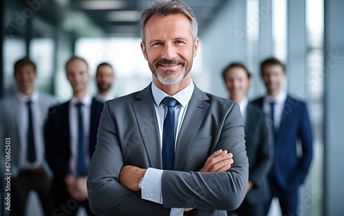Portrait of successful senior businessman standing with his arms crossed businessman and businesswoman over big group of businesspe. Caucasian male entrepreneur in suit looking at camera with a smile.