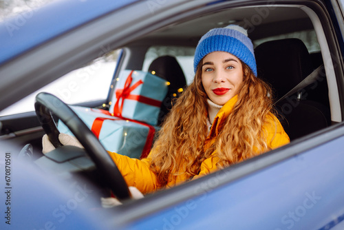A beautiful woman driving a car carries New Year\'s gifts along a snowy road. Happy woman giving gifts. On the eve of the winter holidays, preparation. Shopping concept.