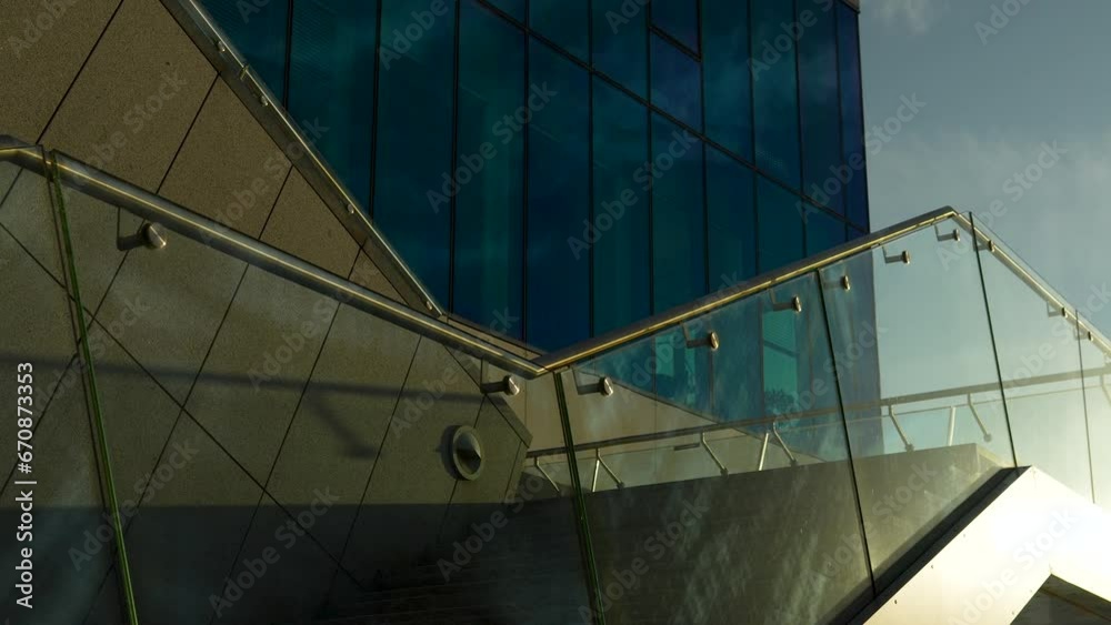 Modern building with blue-tinted windows and sleek glass railing under a sunlit sky. Modern building with blue-tinted windows and sleek glass railing under a sunlit sky.
