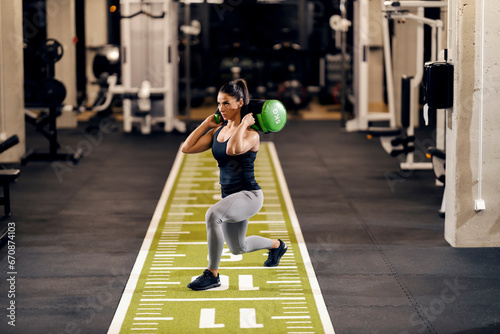 Tableau sur toile A motivated sportswoman is doing lunges while holding weights on her shoulders in a gym