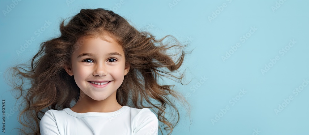 Joyful girl with rosy cheeks wearing summer attire stands happily with arms crossed against blue backdrop