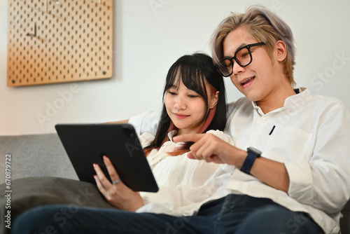 Relaxed young couple browsing internet on digital tablet while sitting on sofa at home