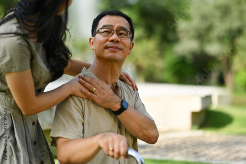 Happy middle aged asian father touching daughter hand on shoulder looking and talking together at the park