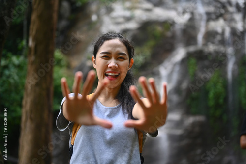 Portrait of happy young woman tourist with backpack standing in front of the tropical waterfall