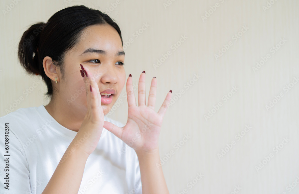 Young Asian woman with open mouths raising hands screaming announcement isolated on light beige background. Young Asian woman with open mouths raising hands screaming announcement isolated on light beige background.