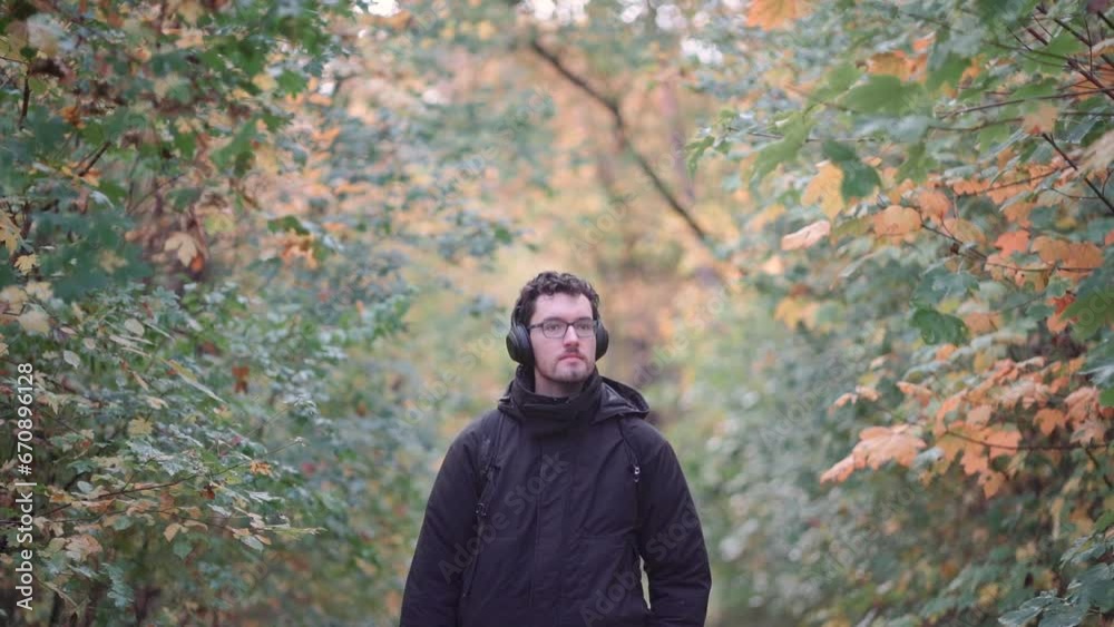 Young European man with headphones in a vibrant fall mixed forest, observing colorful autumn leaves Young European man with headphones in a vibrant fall mixed forest, observing colorful autumn leaves
