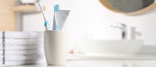 Plastic toothbrushes, toothpaste and towels on white table in bathroom, space for text. Banner design