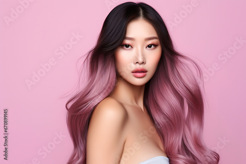 Beautiful, young Asian girl with fresh clean skin, long, dyed pink hair posing on a pink background