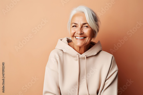 Smiling senior woman posing in beige hoodie on peach background