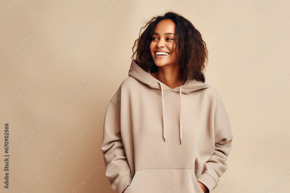 Smiling African American woman with short curly hair posing in a beige hoodie against a beige background. Athleisure style