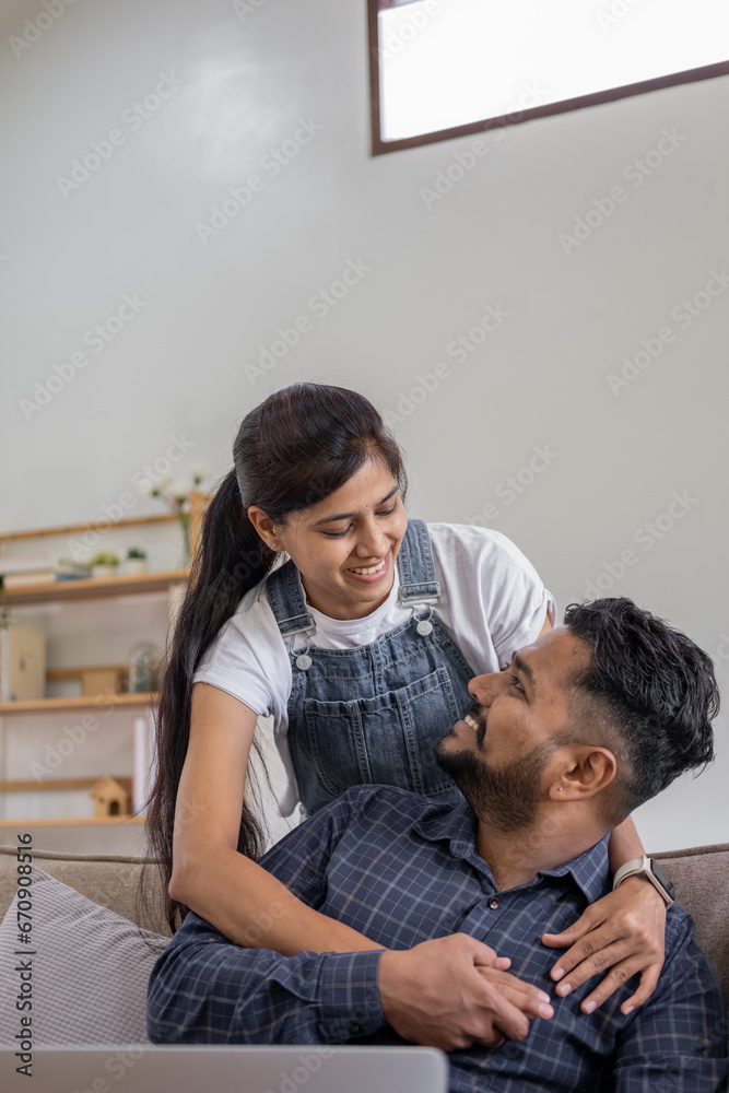 Happy Indian young couple using playing laptop computer notebook on sofa home house Happy Indian young couple using playing laptop computer notebook on sofa home house