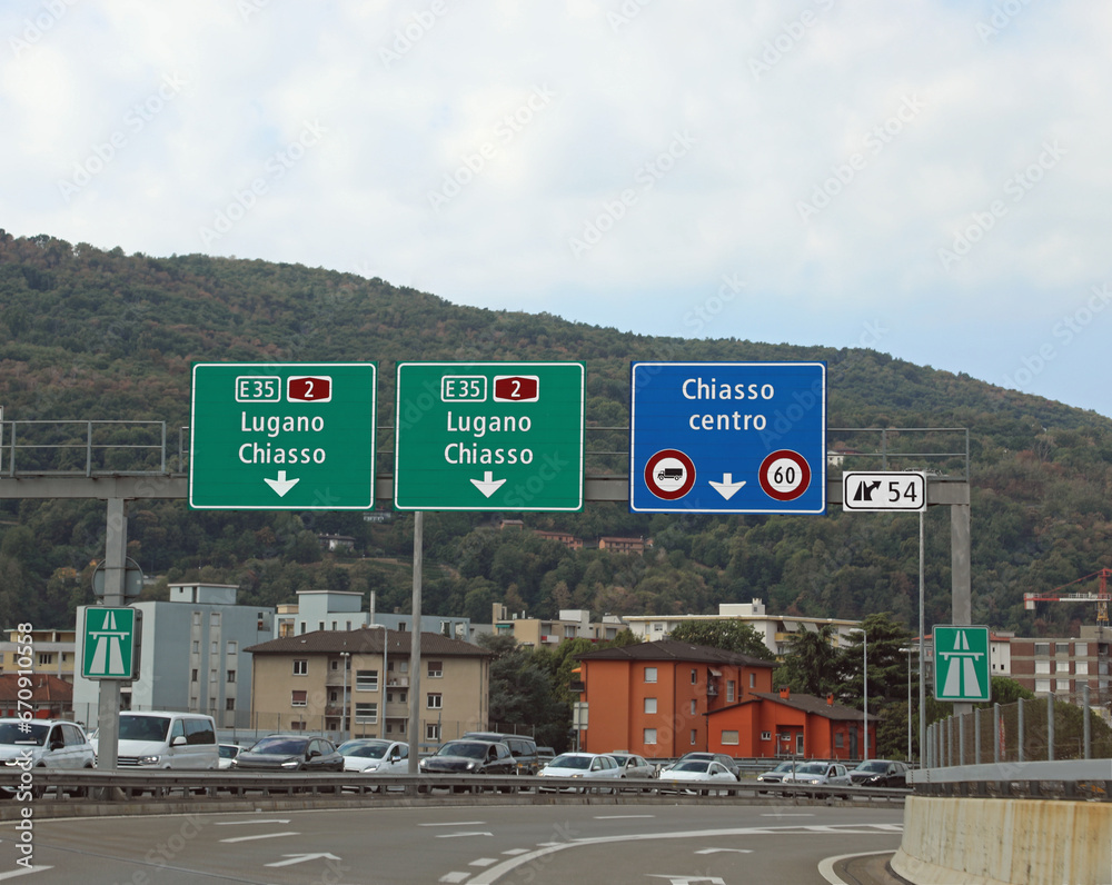 road signs for the cities of CHIASSO and Lugano near the border between Switzerland and Italy