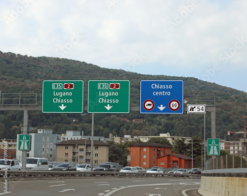 road signs for the cities of CHIASSO and Lugano near the border between Switzerland and Italy